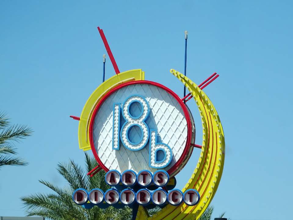 Round neon 18b Arts District sign with a yellow arrow, palm trees below