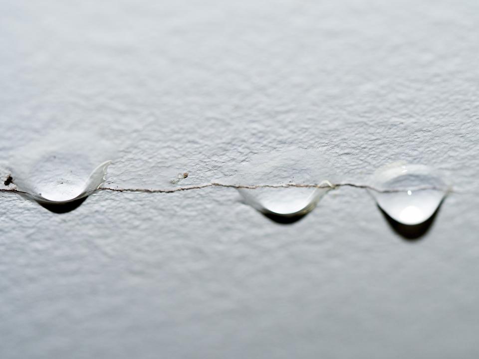 Water drops hanging from a thin crack in a white textured ceiling