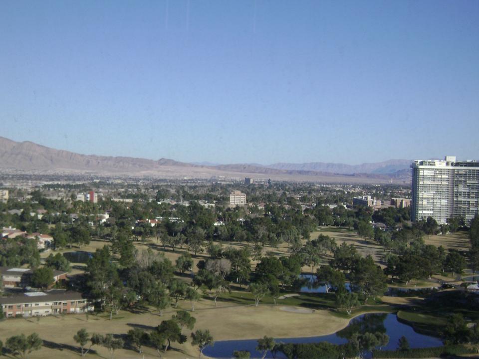 View from a high window over green fairways, ponds and low buildings toward the mountains