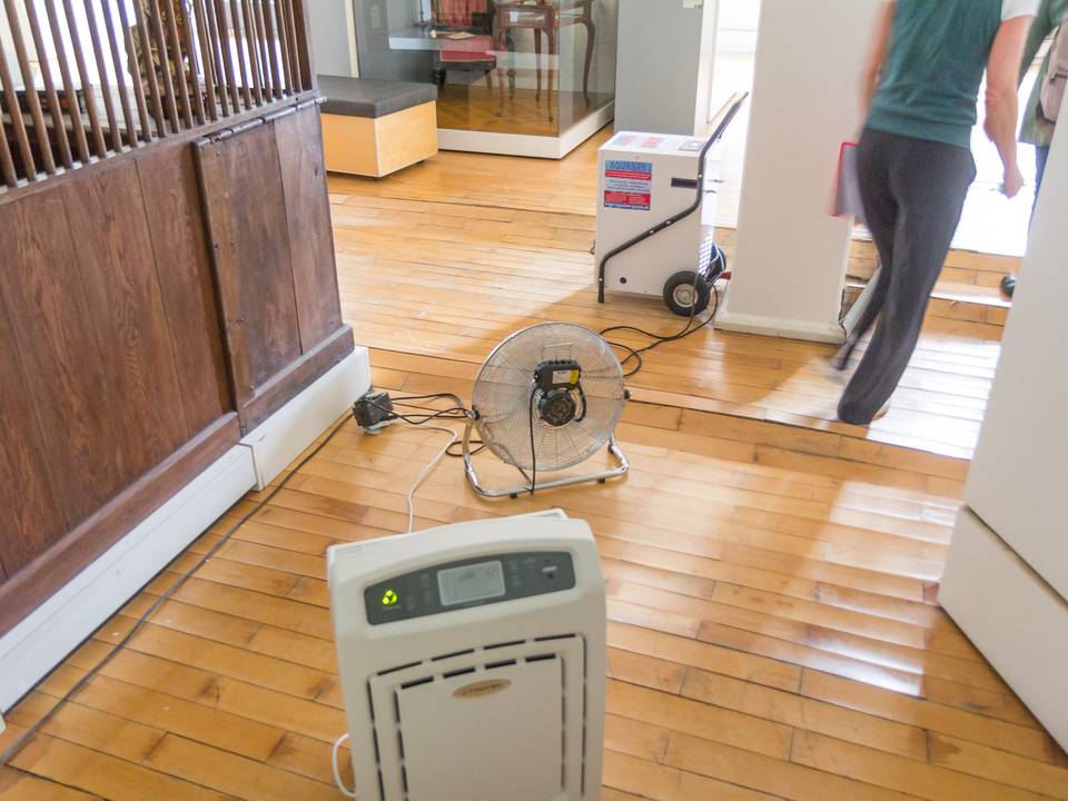Swollen wood parquet floor with a dehumidifier and a floor fan running, a person walking past
