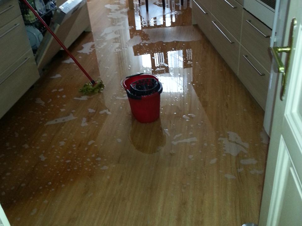Standing water across a wood kitchen floor with a mop and a red bucket