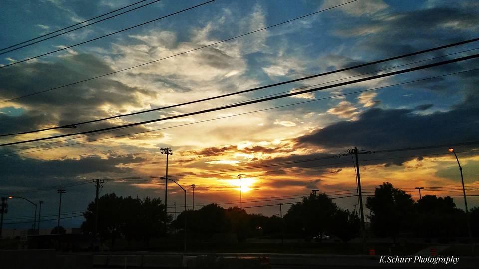 Orange sunset under heavy broken storm clouds, power lines and palm trees in silhouette