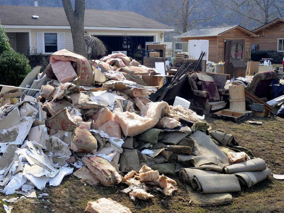 A large pile of wet pink insulation, drywall and rolled carpet on a front lawn